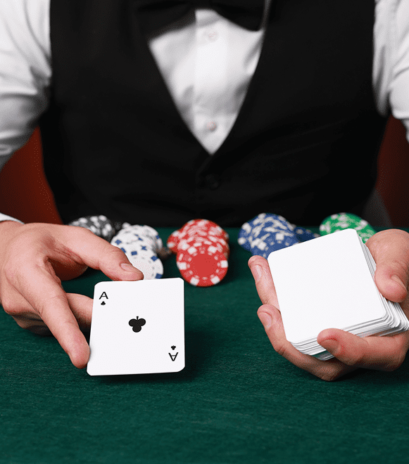 A dealer holding playing cards and poker chips at a casino table.