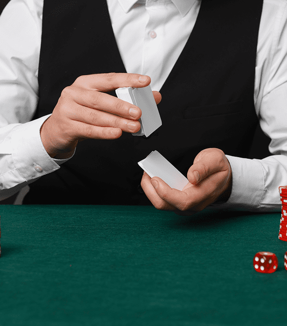 A dealer shuffles playing cards at a casino table with chips and dice nearby.