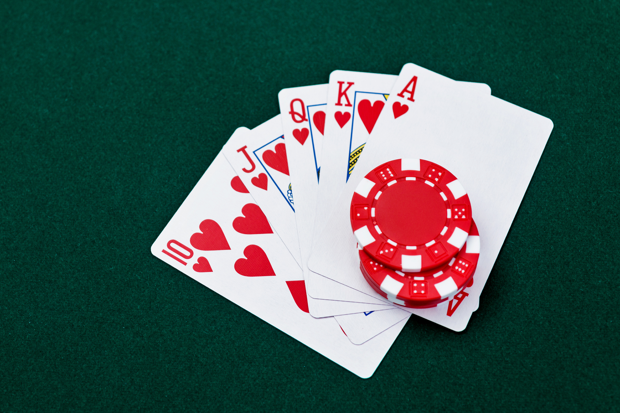 A winning royal flush of hearts with poker chips on a green table.